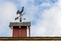 Copper rooster weathervane on top of red rooftop cupola with a blue sky and white clouds in the background