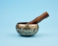 Copper singing bowl and wooden stick on a blue background, a Tibetan musical instrument