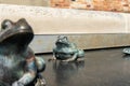 copper statue of a frog in the third stage of life with adult frog blurred in foreground Royalty Free Stock Photo