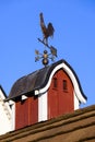 Copper weathervane on red barn cupola, blue sky background.