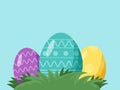 Three colorful Easter eggs are nestled in grass against a light blue background. Royalty Free Stock Photo