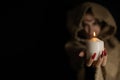 Copy space. On Halloween night, a hooded witch laughs and holds out a burning candle from the darkness. The witch Royalty Free Stock Photo