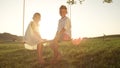 COPY SPACE LENSE FLARE: Little boy and girl sitting on swing smiling at camera