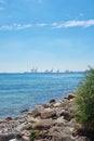 Copy space at the sea with a blue sky background and harbour cranes at a port in the horizon. Calm ocean waves washing