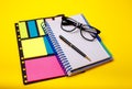 Copybook, glasses, pen and stickers on yellow office background Royalty Free Stock Photo