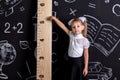 Coquette schoolgirl standing before the chalkboard as a background pointing to the huge scale