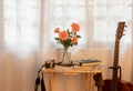 Coral pink roses in a vase, on the table there are books and notebooks, eyeglasses. and a film camera decorated with a brown