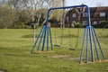 Corby, United Kingdom. April 4, 2019 - outdoor playgroung for children. Spring time, green grass. Empty swing with copy space.