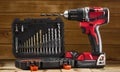 Cordless drill driver in red with rubberized handle in profile with drill bits set