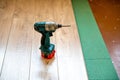 Cordless screwdriver on a laminate floor plank in a room above a green sound-absorbing substrate