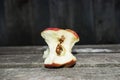 A gnawing Apple with a larva inside lies in the center of the photo on a wooden table