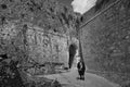 Greyscale shot of a lonely female near the high old building with an arch under the clouds in Greece