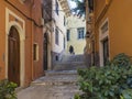 Corfu old town narrow street with older local woman carring bags with shopping purchaise, stairs, doors and windows and flower