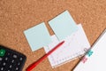 Corkboard desk with a open square paper spiral notebook and office appliances. Billboard table with different sizes and