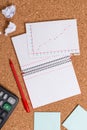 Corkboard desk with a open square paper spiral notebook and office appliances. Billboard table with different sizes and