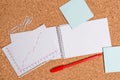 Corkboard desk with a open square paper spiral notebook and office appliances. Billboard table with different sizes and