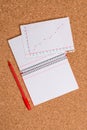 Corkboard desk with a open square paper spiral notebook and office appliances. Billboard table with different sizes and