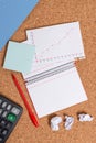 Corkboard desk with a open square paper spiral notebook and office appliances. Billboard table with different sizes and