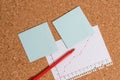 Corkboard desk with a open square paper spiral notebook and office appliances. Billboard table with different sizes and
