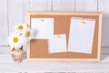 Corkboard for notes with empty paper sheets on a wooden table and next to a clay jar with daisies