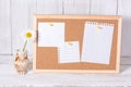 Corkboard for notes with empty paper sheets on a wooden table and next to a clay jar with daisies