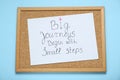 Corkboard with pinned message Big Journeys Begin With Small Steps on light blue background, top view. Motivational quote Royalty Free Stock Photo