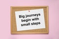 Corkboard with pinned message Big Journeys Begin With Small Steps on pink background, top view. Motivational quote