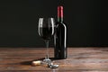 Corkscrew, glass and bottle of red wine on wooden table against black background