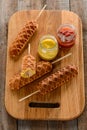 Corn dogs, mustard and ketchup on wooden cutting board