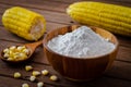 Corn flour in wooden bowl and corn cobs on table