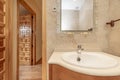 Corner of a bathroom, with a wall of cream-colored marble tiles, a cherry wood cabinet with a porcelain sink, a mirror with a Royalty Free Stock Photo