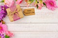 Corner border of flowers with Mothers Day gift and tag against white wood Royalty Free Stock Photo