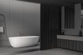 Corner of dark grey bathroom space with wood details and white tub Royalty Free Stock Photo