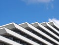 Corner details of a geometric white modern apartment block diagonal geometric balconies and railings against a bright blue sky