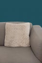 Corner fragment of beige grey upholstered couch with velour decorative cushion on navy blue wall background. 