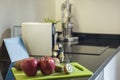 Corner of a kitchen with a black stone countertop with a white capsule coffee machine, designer juicer and a green Teflon board