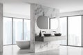 Corner of modern bathroom with double sink and white bathtub, large panoramic window, city view, minimalistic marble and concrete Royalty Free Stock Photo