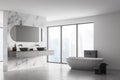 Corner of modern bathroom with double sink and white bathtub, large panoramic window, city view, minimalistic marble and concrete Royalty Free Stock Photo