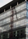 The corner of a modern glass and black office building with reflection of a construction crane on the windows and blue sky Royalty Free Stock Photo