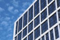 Corner of a modern glass office building next to a blue sky with white clouds Royalty Free Stock Photo