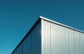Corner of modern warehouse building with corrugated metal wall, blue clear sky. Sunlight reflection on surface. Low angle view of Royalty Free Stock Photo
