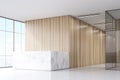 Corner of an office hall with a marble reception counter, wooden walls and a panoramic window.