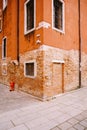Corner of an orange red brick building. The second floor is plastered, the first floor is bare brick. Brick front door