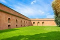 Corner red brick wall of old building, green lawn and a tree against a background of blue sky and white clouds Royalty Free Stock Photo