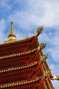 The corner of the red multi-level roof of the pagoda, decorated with gold, against the blue sky with light white clouds Royalty Free Stock Photo