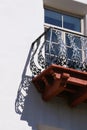Corner of scrolled black wrought iron picket and terra cotta balcony with window on white wall