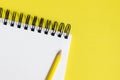 Corner of a spiral bound notepad / sketchpad on a yellow background, with a yellow pencil and space for copy
