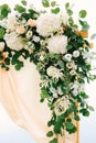 Corner of a wedding arch decorated with satin, flowers and green leaves