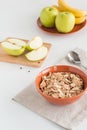 Cornflakes in bowl with fresh apples cut in pieces, bananas, wooden board on white background