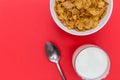 Cornflakes breakfast cereal bowl with milk and spoon on red back
